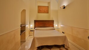 Habitación de hotel con cama, mesitas de noche, cabecero de madera, un cuadro en la pared y suelo a cuadros.