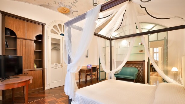 Un dormitorio con cama con dosel, un armario de madera, un escritorio con silla y un televisor.