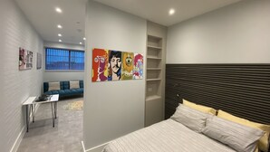 Ein modernes Schlafzimmer mit einem Bett, einer Couch, einem kleinen Tisch und einer Wand mit farbenfrohen Kunstwerken.