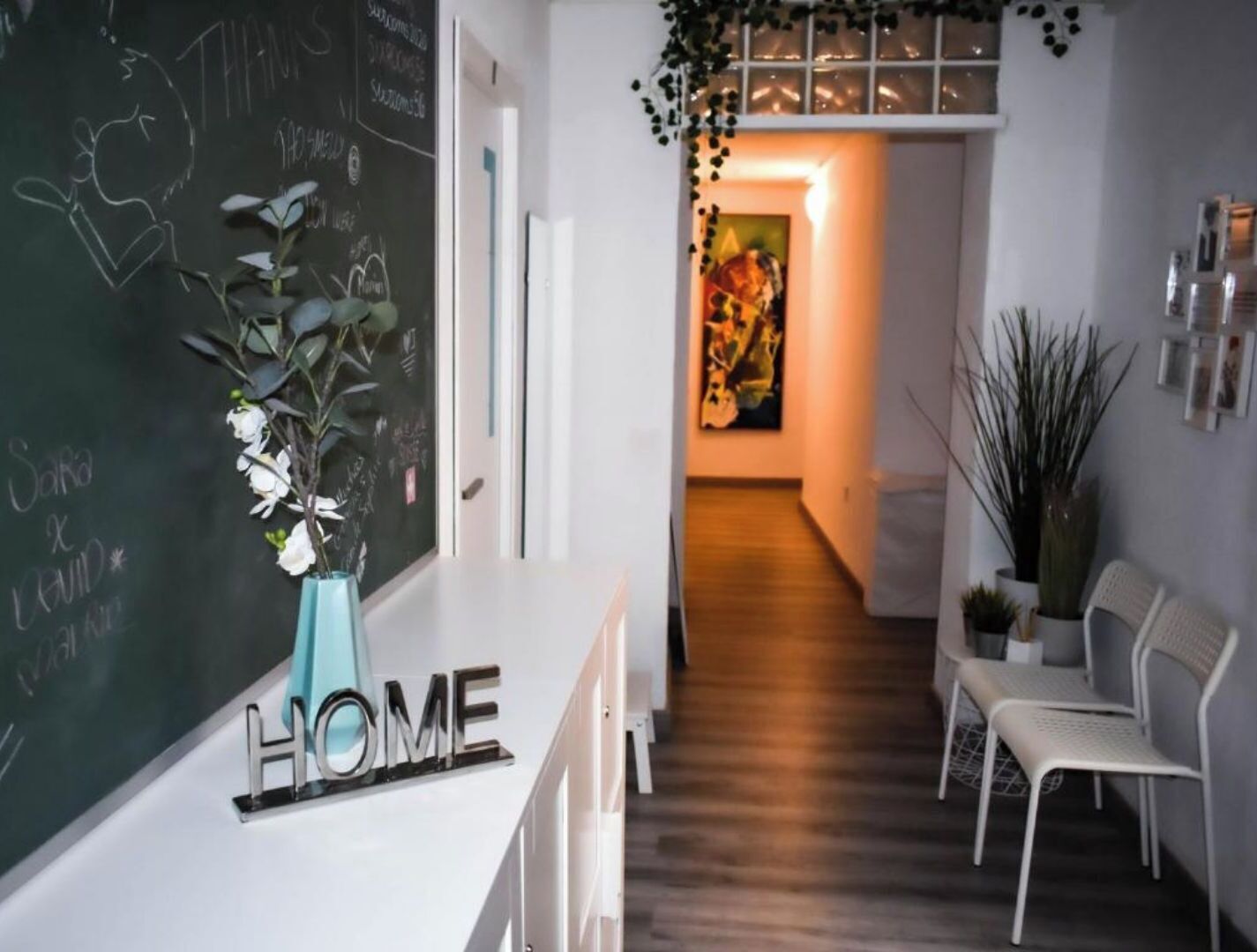 Ein modernes Interieur mit einer Rezeption mit der Beschriftung „HOME“, einer Tafel mit Schrift darauf und einem Flur, der zu einem Raum mit einem Gemälde führt.