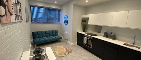 A modern kitchen with a black and white color scheme, a built-in oven, a microwave, and a sink. There is a blue sofa and a small table with plates and a napkin.