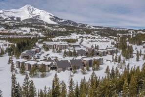 Une station de ski enneigée, composée de plusieurs bâtiments, avec une piste de ski et une montagne en arrière-plan.