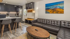 A modern kitchen with dark cabinets, a stainless steel refrigerator, and a bar area with stools. - Newly remodeled studio w/gorgeous mountain views near Big Sky Resort - Hill Condo Lookout (Big Sky)
