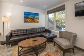Un salon moderne avec un canapé d’angle, une table basse ronde et un fauteuil gris.