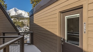 A modern building with a wooden exterior, a visible door with a number plate, and a view of snow-capped mountains in the background. - Newly remodeled studio w/gorgeous mountain views near Big Sky Resort - Hill Condo Lookout (Big Sky)