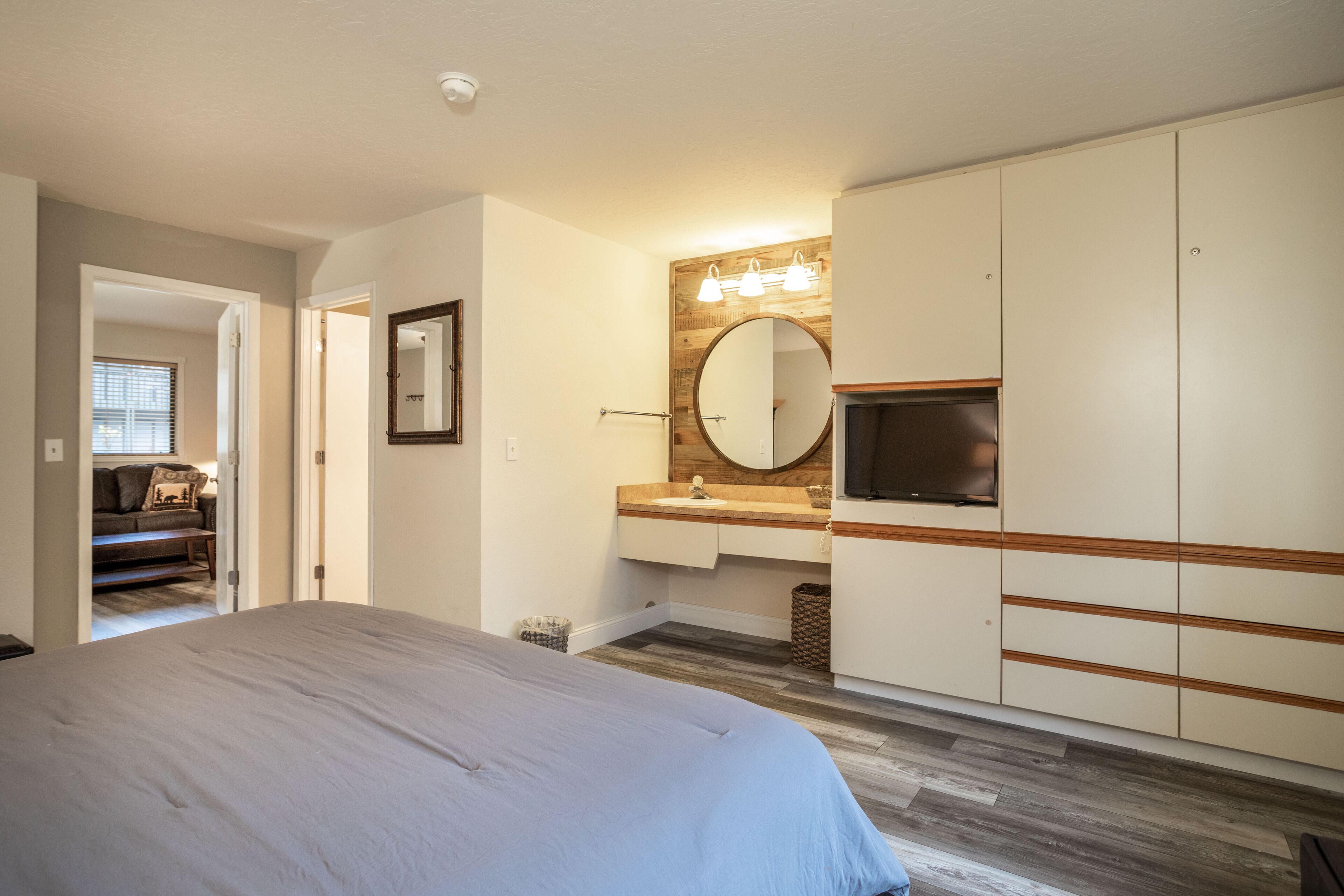 A bedroom with a bed, a vanity with a mirror, and a television.