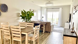 Una sala moderna con comedor, que incluye una mesa y sillas de madera, una planta grande y un sofá.