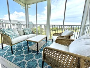 A covered outdoor seating area with wicker furniture, a patterned rug, and a view of a residential neighborhood.