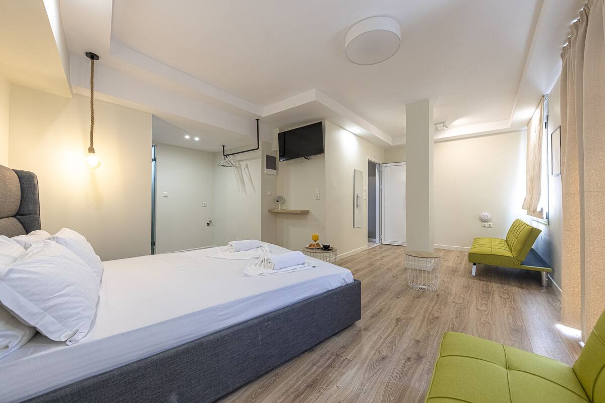 A modern hotel room with a large bed, a green armchair, a small table, and a TV mounted on the wall.