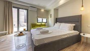 Quarto de hotel moderno com uma cama grande, uma mesa redonda pequena com uma bebida, um sofá verde e uma varanda com vista.