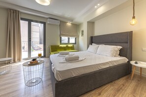 Una habitación de hotel moderna con una cama grande, una pequeña mesa redonda con una bebida, un sofá verde y un balcón con vistas.