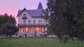 Ein großes, historisches Gebäude mit einem steilen Satteldach und zahlreichen Fenstern, umgeben von einem gepflegten Rasen und Bäumen.