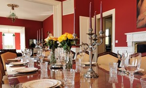 Een elegante eetzaal met een lange tafel, gedekt voor een maaltijd, met kristalglas, borden en een kandelaar met kaarsen.