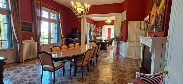 Un comedor con una mesa larga, sillas, chimenea y una araña.