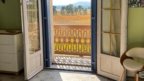 Ein Zimmer mit einer Schiebetür, die auf einen Balkon mit Blick auf ein Feld und Bäume führt.