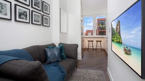 A modern living room with a grey sofa, teal cushions, and a large framed picture of a tropical beach. - Stylish Studio Near Kings Cross Train Station (Elizabeth Bay)