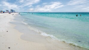 Ein Strand mit klarem türkisblauem Wasser, einem sandigen Ufer und einer entfernten Skyline der Stadt.