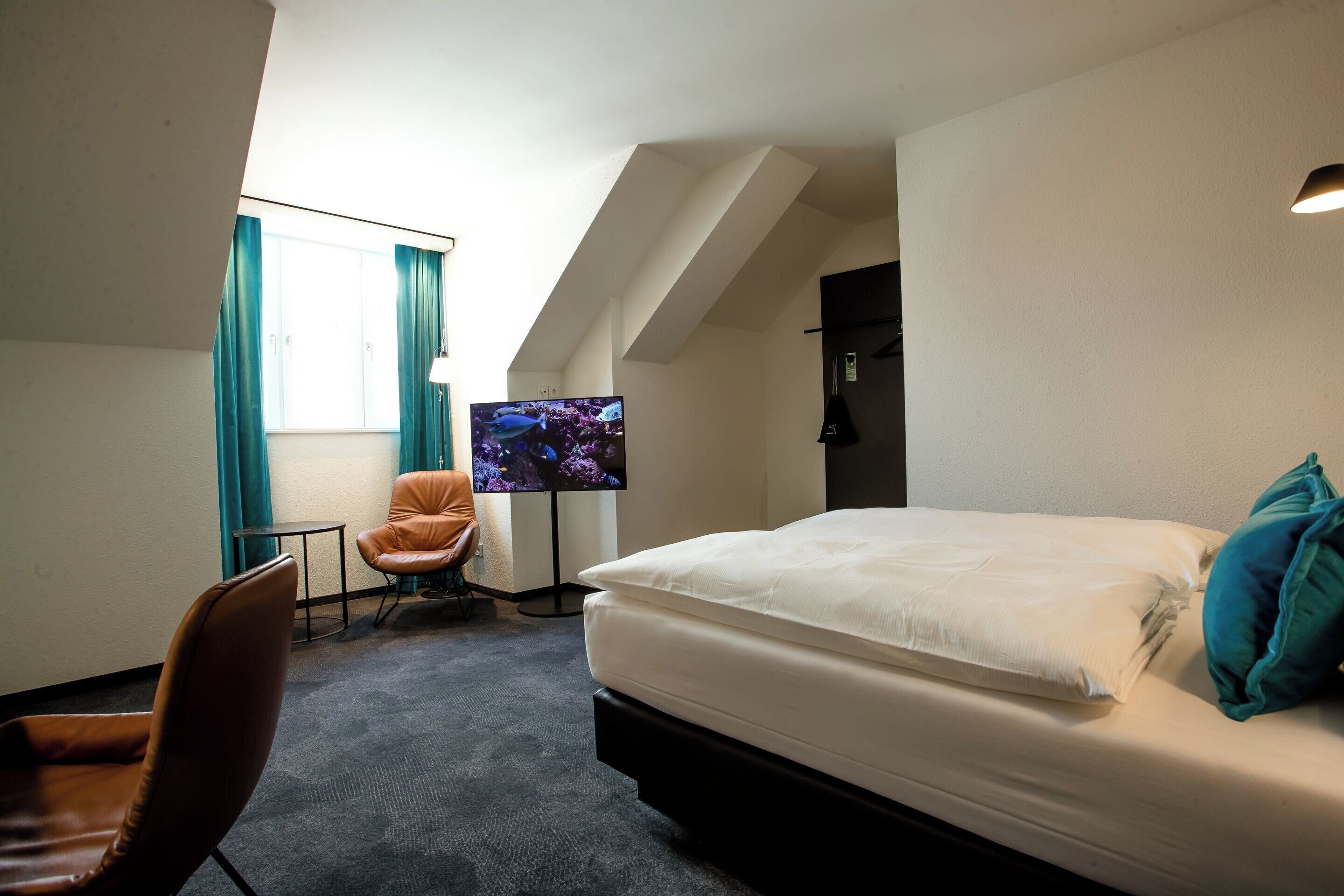 A hotel room with a bed, a chair, a TV, and a window with curtains.