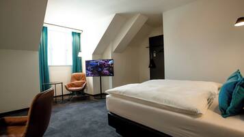 A hotel room with a bed, a chair, a TV, and a window with curtains.