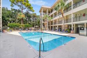 A swimming pool with lounge chairs and a multi-story building with balconies.
