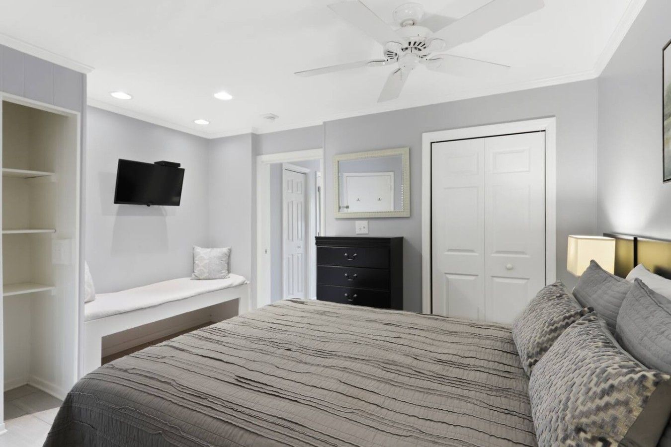 Une chambre à coucher avec un lit, une commode, un téléviseur et un ventilateur de plafond.