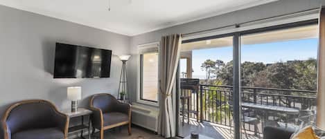 A hotel room with a balcony, a flat-screen TV, a desk, two chairs, and a sofa.