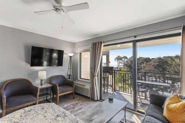 A hotel room with a balcony, a flat-screen TV, a desk, two chairs, and a sofa.