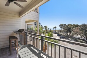 A balcony with a table and chairs, overlooking a parking area and beach with palm trees.