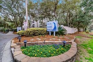 A sign for Sea Side Villas with a landscaped area featuring a flower bed and a fence.