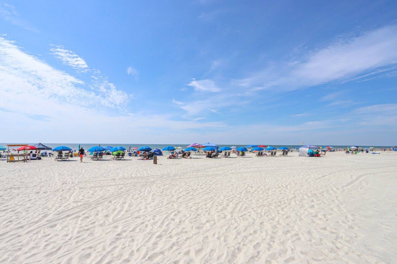 Ein sandiger Strand mit Reihen von Liegestühlen und Sonnenschirmen, ein klarer Himmel und das Meer im Hintergrund.