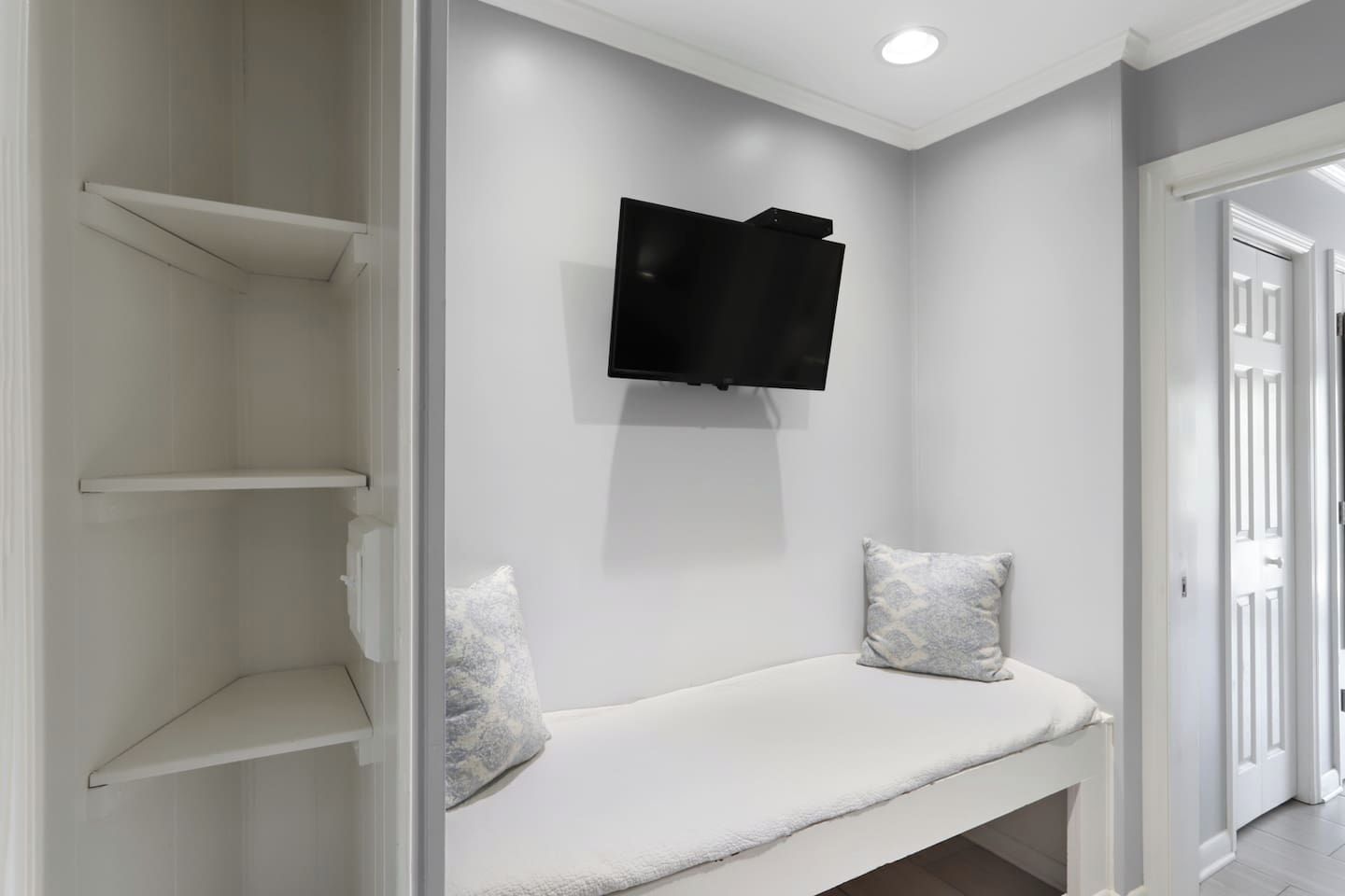 A hallway with a white bench, a mounted flat-screen TV, and a door on the right.