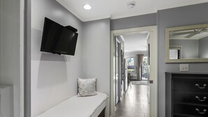 A hallway with a bench, a television mounted on the wall, a dresser with drawers, and a mirror. - Soak Up the Ocean Air Seaside Villa Stay Near the Sand (Hilton Head Island)