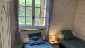 Une petite chambre agréable, dotée d’un lit simple, d’une table de chevet avec une lampe et d’une fenêtre avec des rideaux.