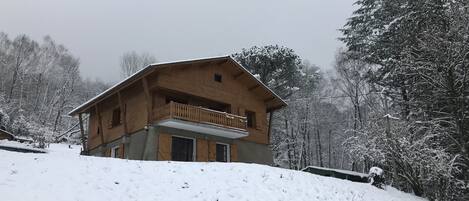 A wooden chalet with a balcony, surrounded by snow-covered trees.
