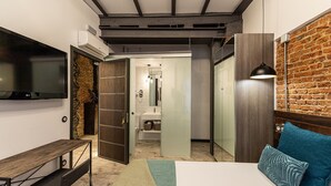 A modern bedroom with a large bed, a TV, a desk, and a brick wall. - Waou Boutique SOL I (Madrid)