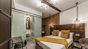 Een moderne slaapkamer met een groot bed, een bureau, een stoel, een douche en een bakstenen muur.