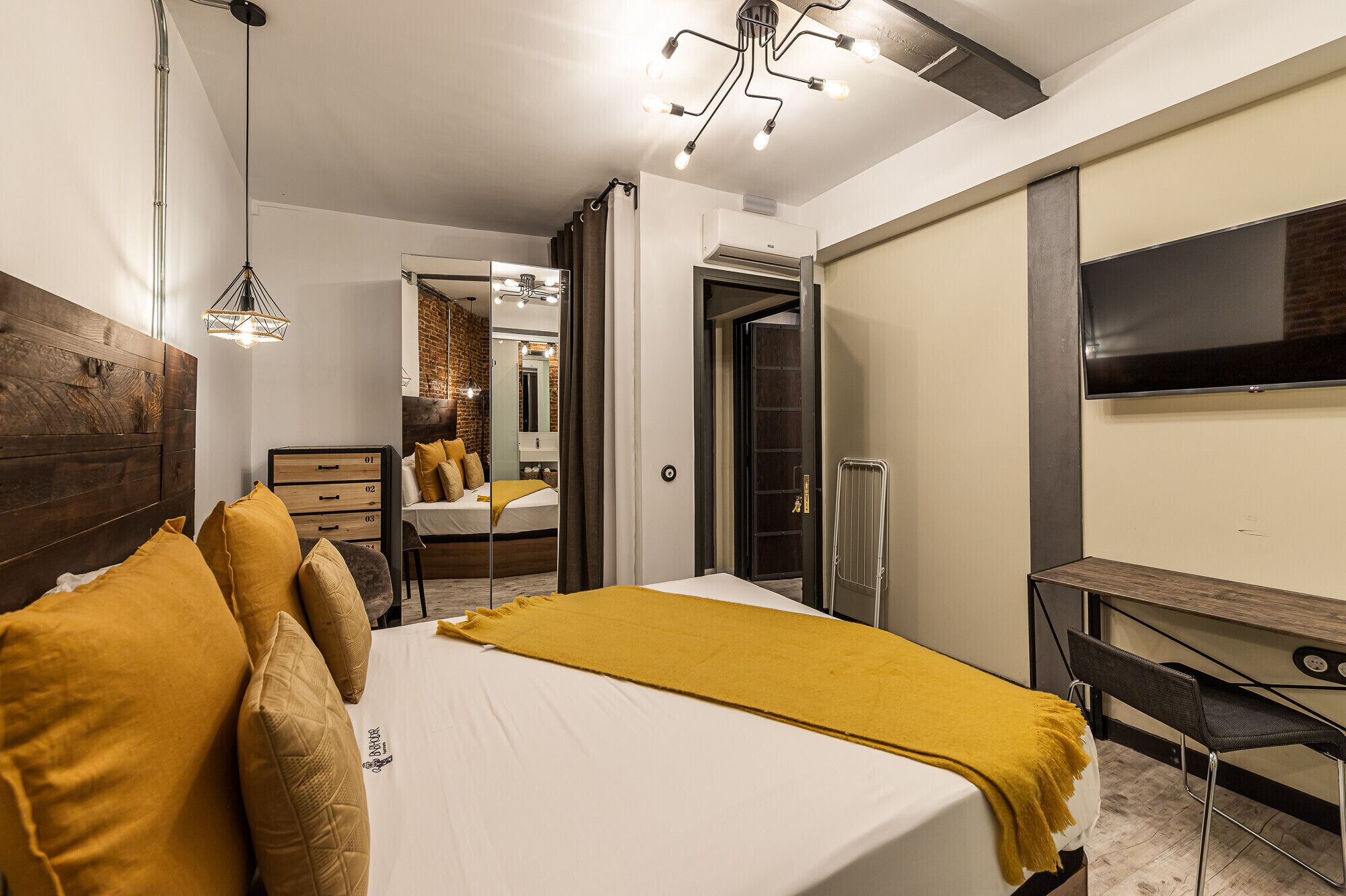 Een moderne slaapkamer met een groot bed, een bureau, een spiegel en een televisie.