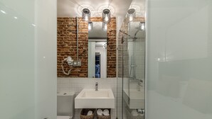 Een moderne badkamer met een accentmuur van baksteen, een douchecabine van glas en een witte wastafel met spiegel erboven.