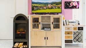 A living room with a fireplace, a television mounted on a cabinet, and a clock on the wall. - 🌸 5-star luxury "Orchidee": Your private spa resort on 85 m² (Arnbruck)