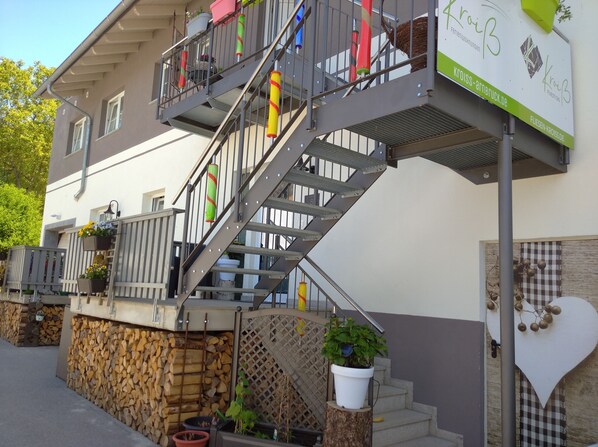 A multi-story building with a metal staircase, outdoor seating area with potted plants, and a signboard.