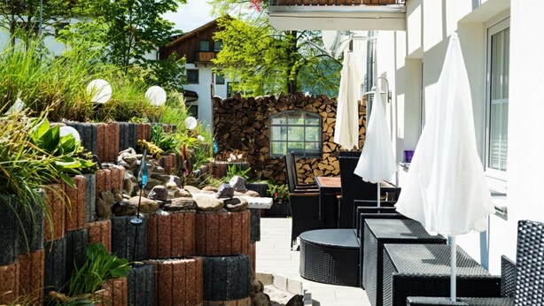 A patio area with outdoor seating, a stone wall, and a window overlooking greenery. - 🌸 5-star luxury "Orchidee": Your private spa resort on 85 m² (Arnbruck)