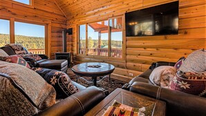 A cozy log cabin interior with leather sofas, a round coffee table, and large windows offering a view of the forest. - Spectacular Views, Hot Tub, Close to Wolf Creek & San Juan River (Pagosa Springs)