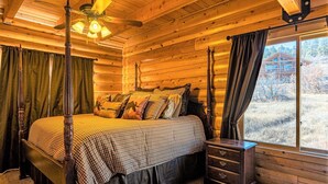 A log cabin bedroom with a four-poster bed, a nightstand, a dresser, and a window with curtains. - Spectacular Views, Hot Tub, Close to Wolf Creek & San Juan River (Pagosa Springs)