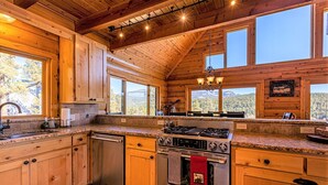A spacious kitchen with wooden cabinets, granite countertops, a stainless steel stove, and large windows offering scenic views. - Spectacular Views, Hot Tub, Close to Wolf Creek & San Juan River (Pagosa Springs)