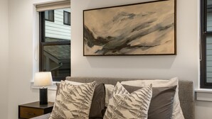 A bedroom with a bed, two pillows with fern patterns, a nightstand with a lamp, and a painting on the wall.