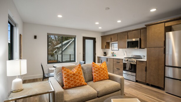 A modern kitchen with stainless steel appliances, a dining area with a glass table, and a sofa with patterned cushions.