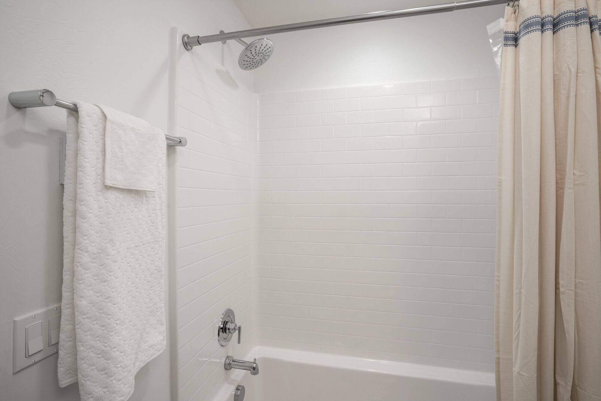 A white tiled shower with a glass door, a towel rack, and a showerhead.