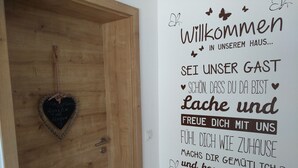 Eine Holztür mit Herzdeko und eine Wand mit einer Begrüßung auf Deutsch.