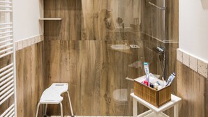 Eine Dusche mit Holzwand, einem weißen Ablagebrett mit Toilettenartikeln und einem kleinen Hocker.