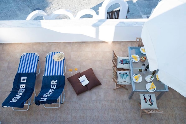 A rooftop terrace with two striped lounge chairs, a small table with plates and glasses, and a white tent-like structure.